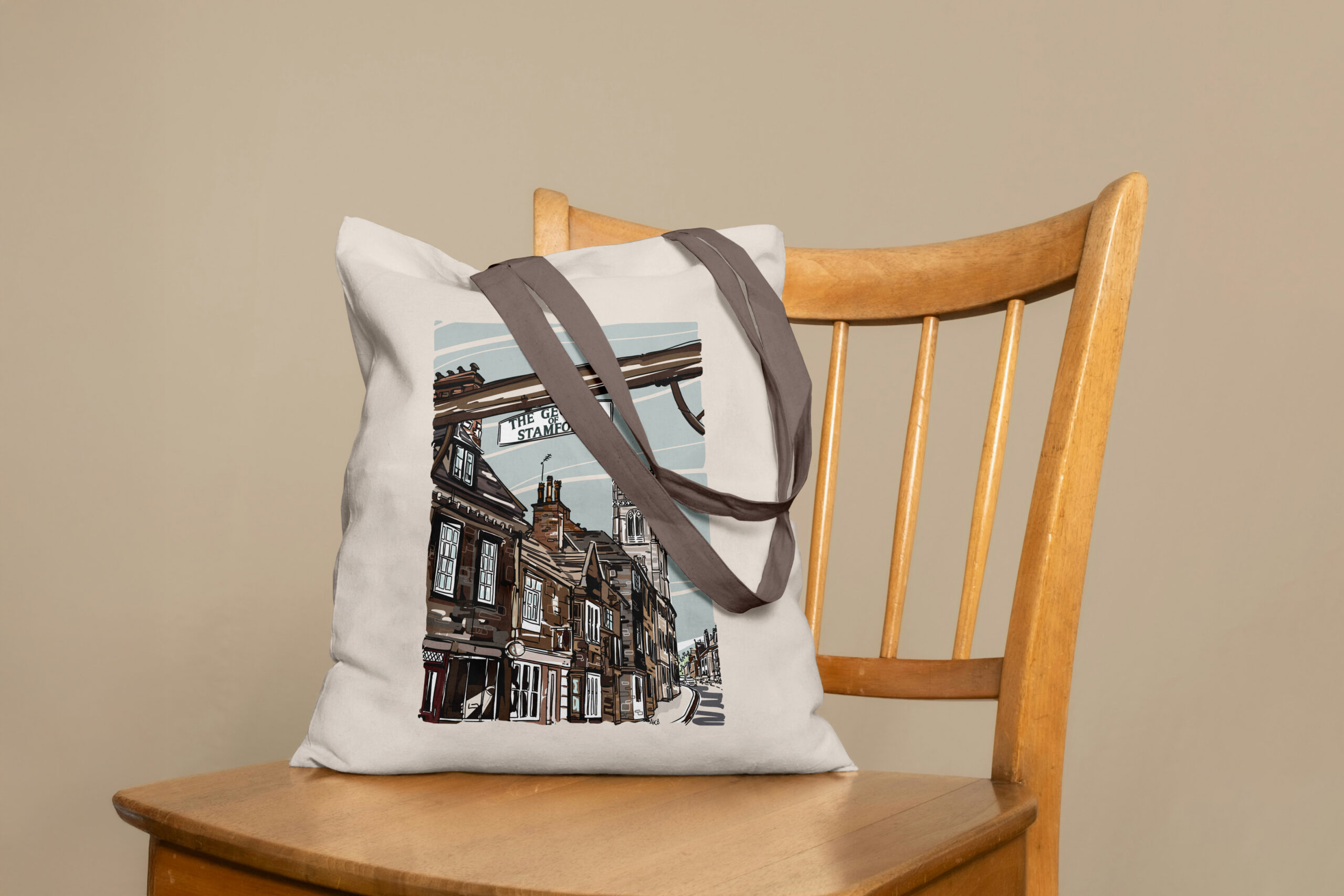 Cream canvas tote bag with a historic streetscape illustration resting on a wooden chair